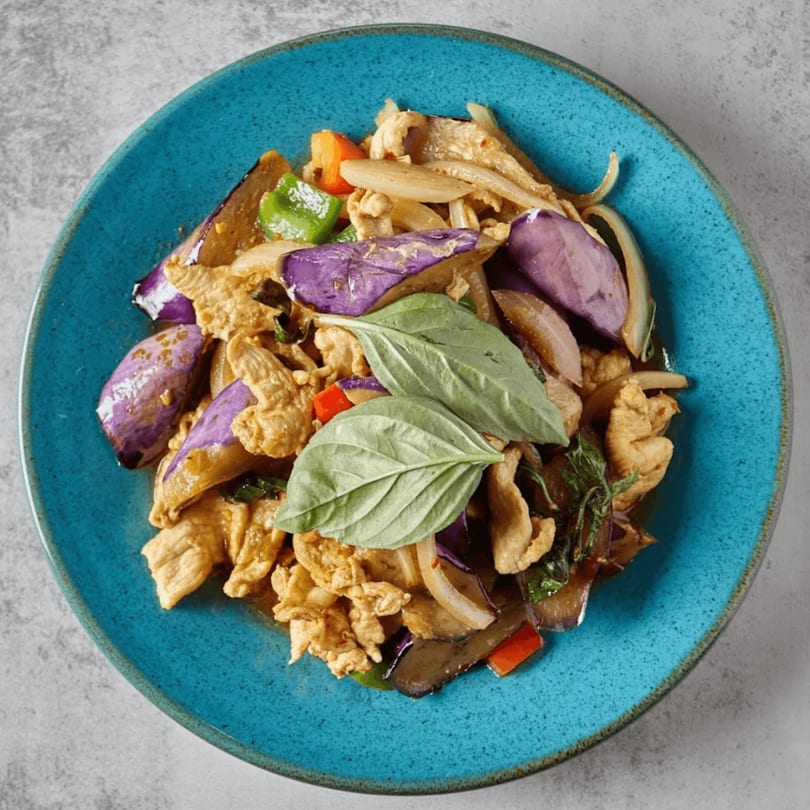 Stir-fried chicken with purple eggplant, onions, bell peppers, and basil on a blue plate.